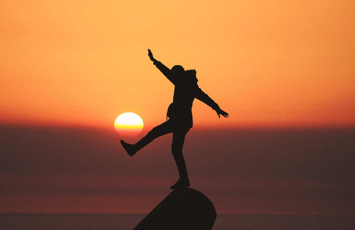 Man balancing on a rock at sunset
